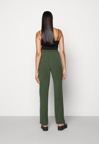 Groene broek met een losse pasvorm en een elastische tailleband, gecombineerd met een zwart aansluitend topje. Gladde textuur, volledig lang ontwerp, en zijnaden.