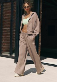 Beige zip-up hoodie med en blød tekstur, parret med løstsiddende beige sweatpants og en lys grøn crop top. Små logo-detaljer er synlige.
