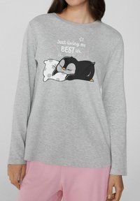 Camiseta de manga larga gris con un pingüino de dibujos animados durmiendo en una almohada de puntos, con el texto "Sólo viviendo mi MEJOR vida" arriba.