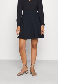 Mörkblå skaterkjol med hög midja, sidoknappar och en slät yta. Tillsammans med svartvita randiga klacksandaler.