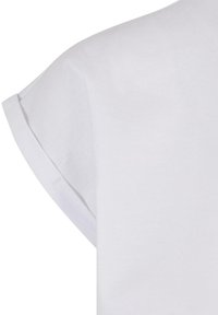 Gros plan d'une chemise blanche à manches courtes montrant l'ourlet replié et la texture lisse du tissu au niveau de l'épaule.