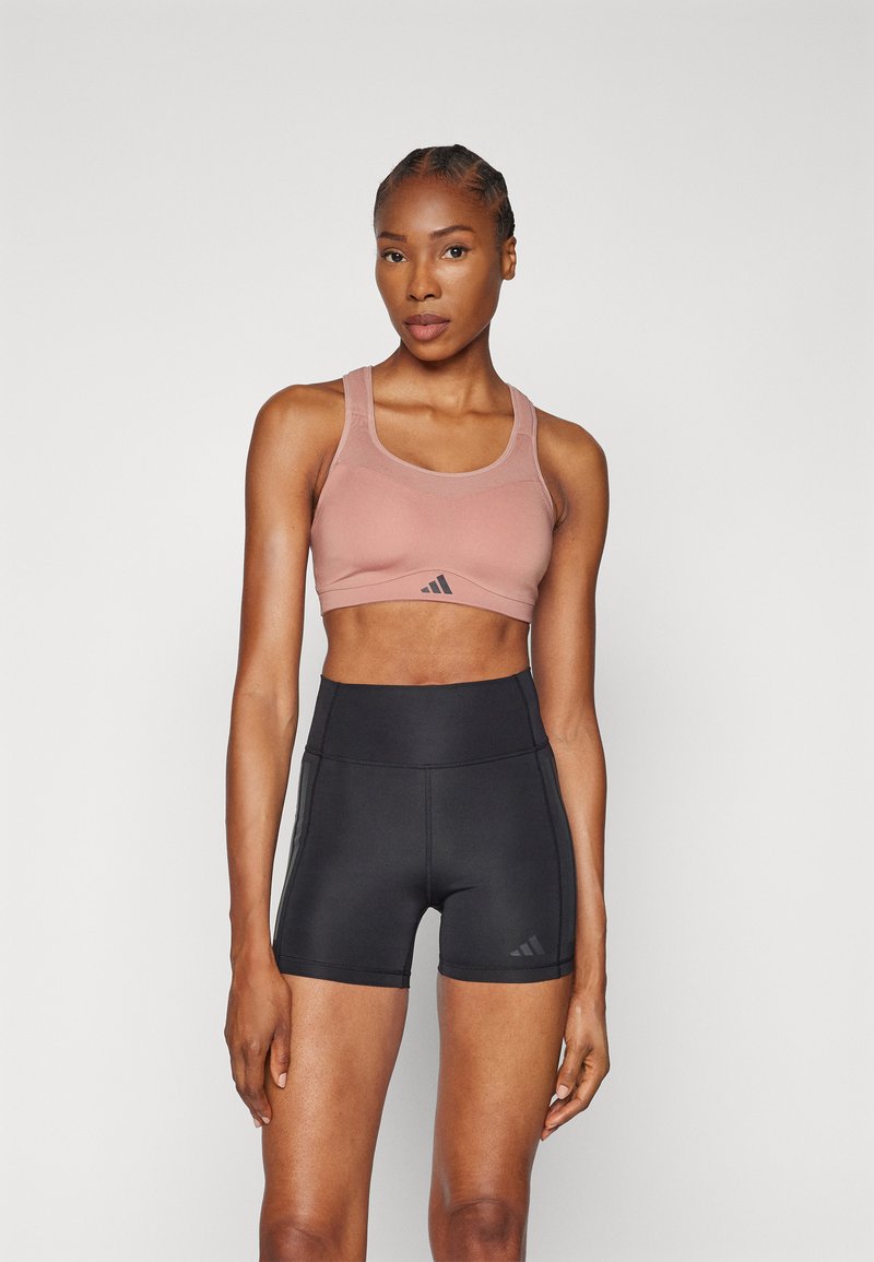 Sorte høytlivs shorts kombinert med en lys rosa sports-bra med en diskret logo. Stoffene ser ut til å være elastiske og tettsittende.