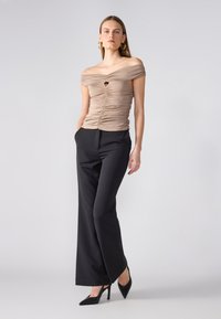 Beige off-the-shoulder tops ar ružām, ar centrālo izgriezumu un melnām augstām platām biksēm, papildināts ar melnām augstpapēžu kurpēm.