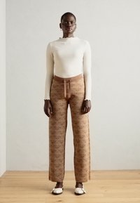 Haut à manches longues blanc à côtes et pantalon large à motif marron avec taille à cordon. Associé à des chaussures blanches à enfiler. Texture lisse, design élégant.