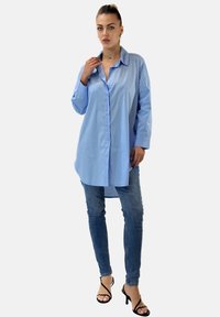 Camicia azzurra chiara in cotone, con colletto a punta, maniche lunghe e vestibilità rilassata. Abbinata a jeans skinny blu scuro.
