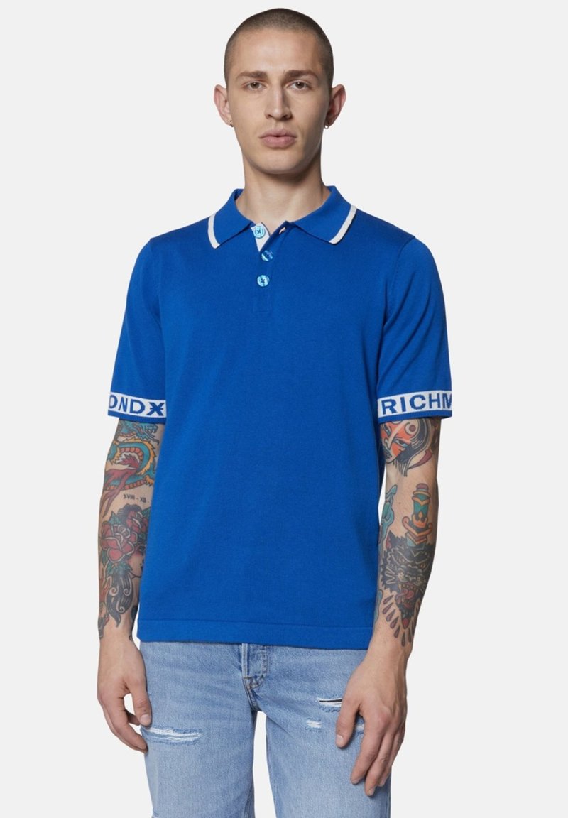 Polo azzurro con colletto e maniche a contrasto bianchi, con logo sulle maniche, abbinato a jeans chiari strappati.