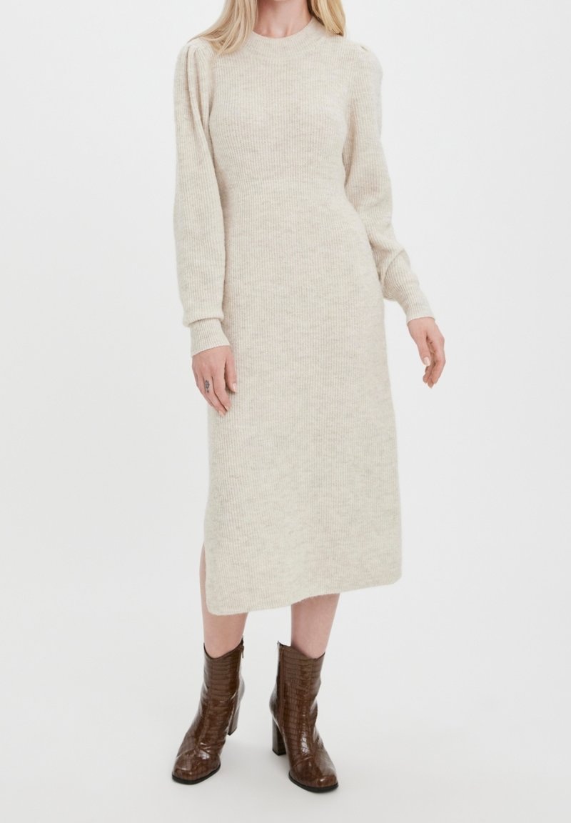 Beige stickad midikjol med lång ärm och rund halsringning, med ribbad textur och en sidofålla. Stylandes med bruna klackstövlar.