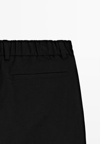 Zwarte broeken met een elastische tailleband en een enkele horizontale achterzak met bies.