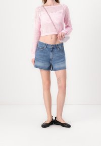 Różowy dzianinowy crop top z motywem motyli, w zestawieniu z niebieskimi szortami dżinsowymi i czarnymi płaskimi butami. Dodatki to mała torebka na ramię.