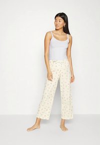 Jasnofioletowy top na ramiączkach z falistymi krawędziami w połączeniu z kremowymi spodniami z szerokimi nogawkami ozdobionymi delikatnym kwiatowym wzorem.