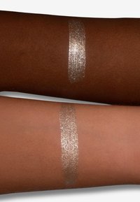 Dos antebrazos con diferentes tonos de piel mostrando una franja vertical de maquillaje brillante plateado metálico en cada uno.