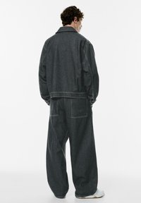 Dark denim jacket and wide-leg pants with a loose fit. Features visible stitching, a collar, and back pockets on the pants.