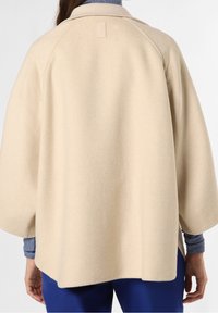 Beige uldblandingsfrakke med raglanærmer, minimalistisk design og et diskret logo-tag ved kraven, med en blød, tekstureret finish.