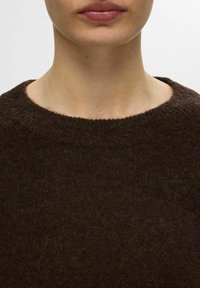 Brauner Wollpullover mit einem gerippten runden Ausschnitt und weicher Textur, der ein leicht flauschiges Aussehen hat. Nahaufnahme des Ausschnittbereichs.