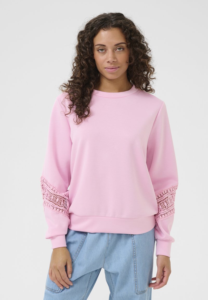 Rožinė džemperis ilgomis rankovėmis su sudėtingu nėriniuotu apdailu ant rankogalių ir apvaliu iškirpimu. Lygus audinio paviršius, laisvas siluetas.