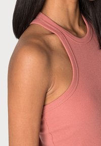 Ribbad, ärmlös topp i mjuk rosa tyg. Har en hög halsringning och rundade ärmhål för en tight passform mot huden.