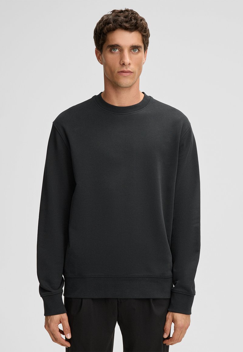 Czarna bluza z okrągłym dekoltem, długimi rękawami i ściągaczami przy mankietach. Wykonana z gładkiego materiału, o luźnym kroju, bez widocznych wzorów.