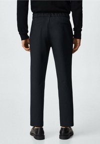 Černé kalhoty s měkkým elastickým pasem, vybavené dvěma zadními kapsami a zúženým střihem, vyrobené z hladké látky. Kombinovány s černými botami.