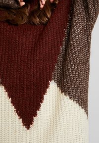 Neulepaita, jossa on kolmiomainen kuvio burgundin, ruskean ja kermaisen värin yhdistelmässä. Ominaisuuksia ovat tekstuuri ja löysä malli.