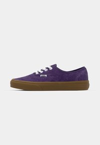Lila mockaskor med vita snörningar, en vadderad krage och en brun gummisula med strukturerade detaljer. Vans-logotyp synlig på sidan.