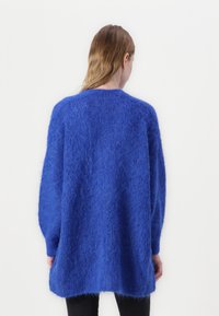 Blå oversized genser med en fluffy tekstur, med lange ermer og rund hals. Plagget har en avslappet passform og faller til midje.