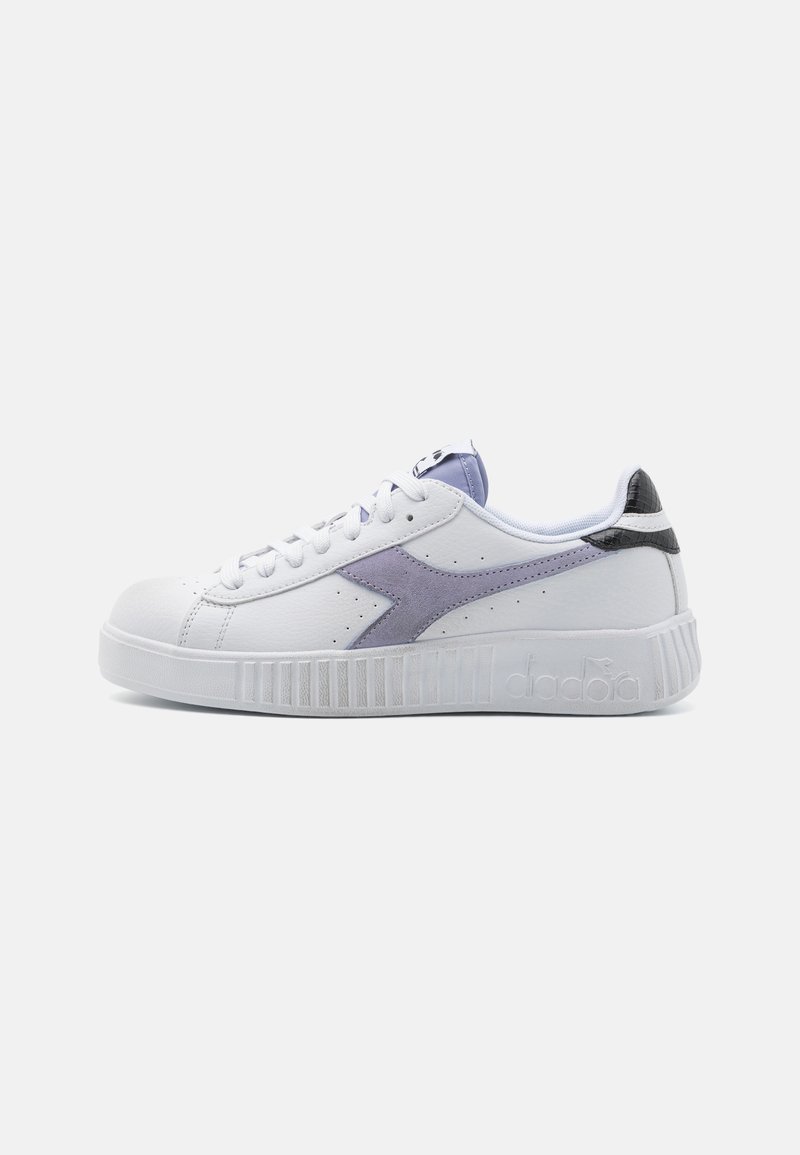 Baskets blanches avec un accent en cuir suédé violet et un talon noir. La semelle en caoutchouc texturé présente des rainures verticales. Fermeture lacée et languette rembourrée.