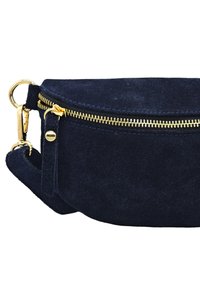 Sac bandoulière en suède bleu marine avec une forme arrondie, fermeture éclair dorée et accents matériels, comportant une bandoulière détachable et une texture douce.