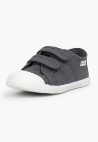 Zapato de tela gris con doble correa de velcro, puntera de goma blanca y suela texturizada. Presenta costuras laterales y un pequeño parche con logo.