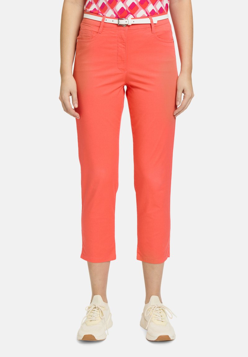 Pantalons courts corail avec une texture lisse et une coupe slim, dotés de poches avant et portés avec une ceinture blanche et des baskets beiges.