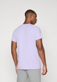Camiseta de manga corta en color lila, hecha de algodón suave, con cuello redondo y un diseño ajustado, vista desde una perspectiva trasera.