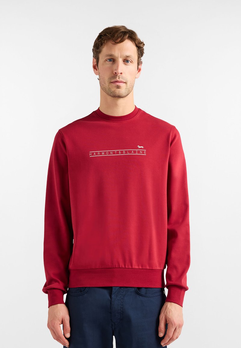 Czerwona bluza z okrągłym dekoltem, długimi rękawami i ściągaczami przy mankietach. Na środku klatki piersiowej znajduje się biały wzór z logo. Miękka w dotyku.