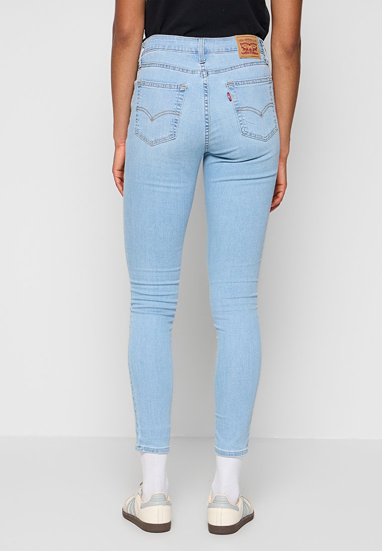 Hellblaue Skinny-Jeans mit glatter Textur, hoher Taille und auffälligen Gesäßtaschen; verfügt über ein Leder-Logopatch am Bund.