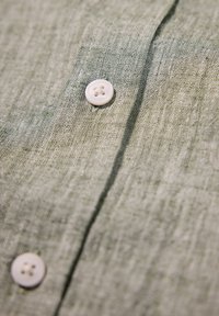 Gros plan d'un tissu texturé gris clair avec deux boutons blancs à quatre trous cousus sur une couture verticale.