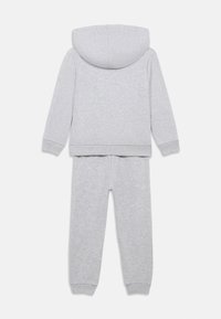 Conjunto de sweatshirts com capuz em cinza claro e calças de jogger a condizer, tecido suave, punhos e cintura canelados, deitado de lado mostrando a parte de trás.