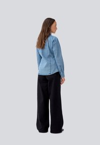Lyseblå denimskjorte med lange ermer, knappede mansjetter og rund hem, sammen med høyhælte, vide svarte bukser.