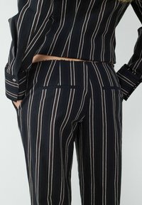 Gestreepte broeken in marineblauw met verticale witte en bordeauxrode strepen. Heeft een getailleerde pasvorm, achterzakken en een gladde, lichte stof.