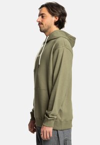 Olijfgroene hoodie met een trekkoordcapuchon, een kangaroo zak en geribbelde manchetten. Zacht, ontspannen pasvorm met minimale merklogo's.