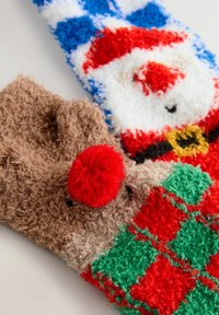 Zwei festliche Socken: Die eine hat ein Weihnachtsmann-Design in Rot, Weiß und Blau; die andere ist braun mit einer roten Pompon-Nase und grünen Akzenten.