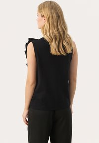 Black sleeveless top featuring textured fabric and ruffle detail on the shoulder. Simple, straight-cut design.