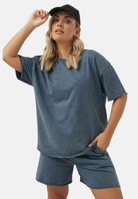 Swobodny strój w stylu dżinsowym, składający się z luźnej, krótkos hirtowej szaro-niebieskiej bluzki i pasujących szortów, wykonanych z miękkiej, teksturowanej tkaniny.