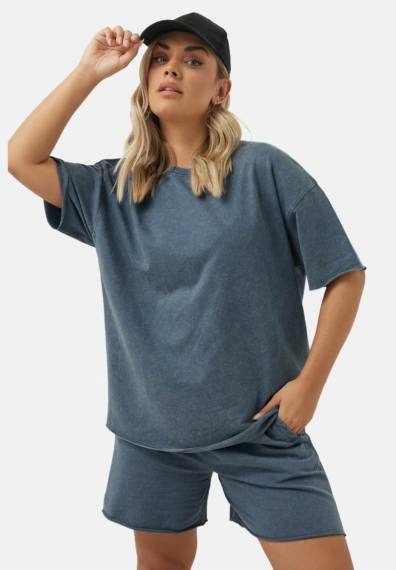 Swobodny strój w stylu dżinsowym, składający się z luźnej, krótkos hirtowej szaro-niebieskiej bluzki i pasujących szortów, wykonanych z miękkiej, teksturowanej tkaniny.