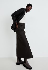Pantaloni largi de culoare maro închis asortați cu un top cu model și o jachetă din piele neagră. Completați cu bottine gri la glezne, cu talpă groasă.