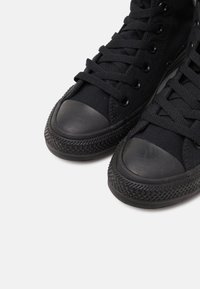 Svart høy-top sneakers laget av lerret med gummikappe, teksturert gummisåle og klassisk snøring med metalløye.