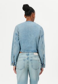 Lichtblauwe spijkerjacket met lange mouwen en een cropped ontwerp, voorzien van een effen textuur en knoopaccenten, gecombineerd met bijpassende jeans.