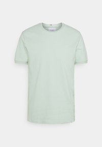 T-shirt en coton vert clair à manches courtes, col rond, avec un petit détail de logo blanc sur la poitrine. Texture lisse, coupe décontractée.
