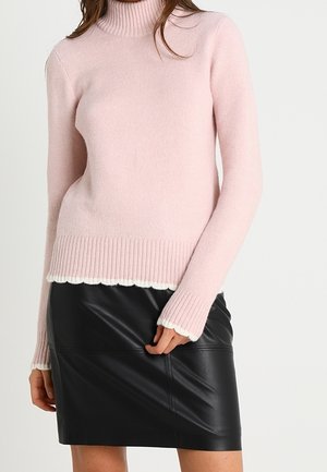Femme portant un pull à col roulé rose clair avec des poignets et un ourlet côtelés, assorti à une mini jupe en cuir noir.