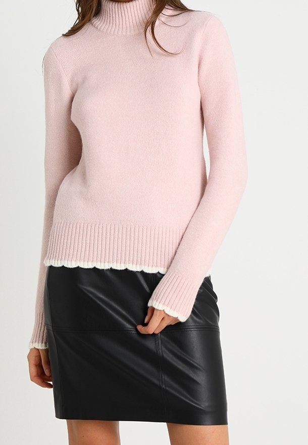Femme portant un pull à col roulé rose clair avec des poignets et un ourlet côtelés, assorti à une mini jupe en cuir noir.
