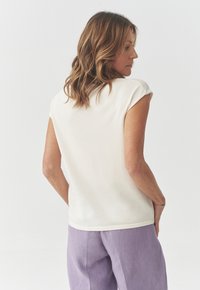 White short-sleeve top with a crew neckline, smooth texture, and a subtle hemline. Paired with light purple linen trousers.