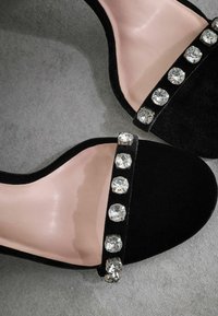 Scarpe con tacco alto in velluto nero, con un interno rosa liscio, caratterizzate da una fila di grandi strass trasparenti lungo la fascetta.