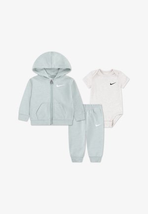 Jasnoszara bluza niemowlęca z kapturem na suwak, pasujące spodnie dresowe oraz biały body z krótkim rękawem, wszystkie z małymi czarnymi lub białymi logo Nike swoosh.